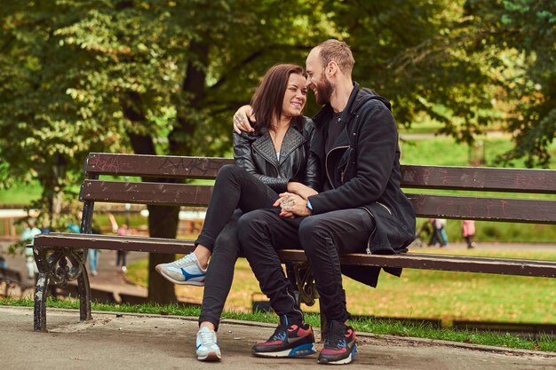 Glückliches modernes Paar, das auf einer Bank im Park kuschelt. Genießen Sie ihre Liebe und Natur.