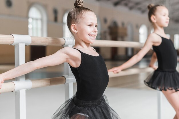 Glückliches nettes Ballerinamädchen, das bei Barre übt