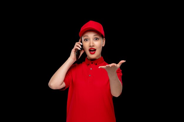 Glückliches nettes Mädchen des roten Hemdtages, das am Telefon in einer roten Kappe spricht, die Hemd und hellen Lippenstift trägt