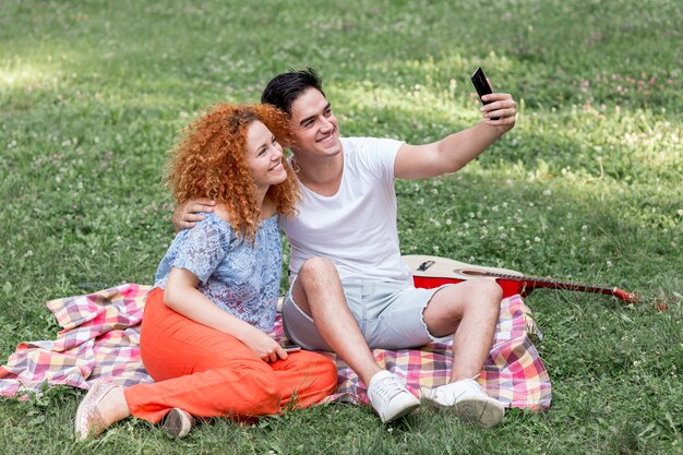 Glückliches Paar, das auf das Gras nimmt ein selfie legt