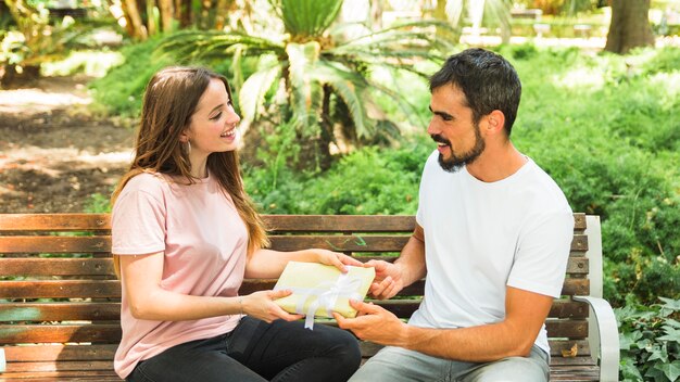 Glückliches Paar, das auf der Bank hält Valentinsgrußgeschenk sitzt