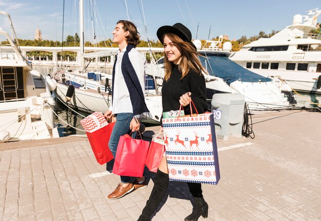 Glückliches Paar, das auf Pier mit Einkaufstaschen geht