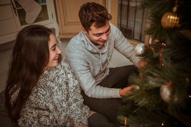 Kostenloses Foto glückliches paar, das den weihnachtsbaum sitzt auf boden verziert