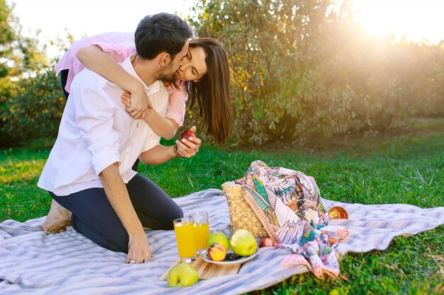 Glückliches Paar, das ein Picknick im Park an einem sonnigen Tag hat, küsst und umarmt