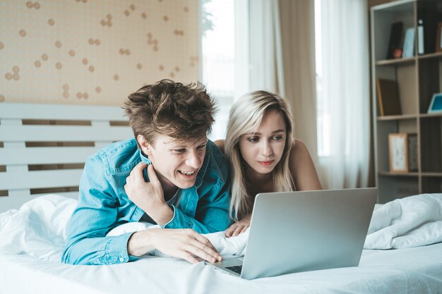 Glückliches Paar, das Laptop-Computer auf dem Bett verwendet