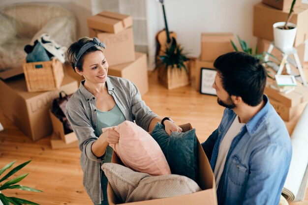 Glückliches Paar, das sich beim Auspacken seiner Zugehörigkeit im neuen Zuhause unterhält