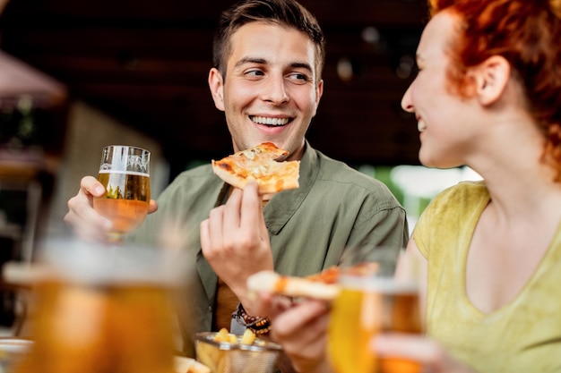 Glückliches Paar, das sich beim Pizzaessen und Biertrinken in einer Kneipe unterhält