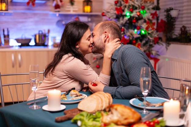 Glückliches Paar, das sich nach dem Heiratsantrag in der Weihnachtsküche küsst