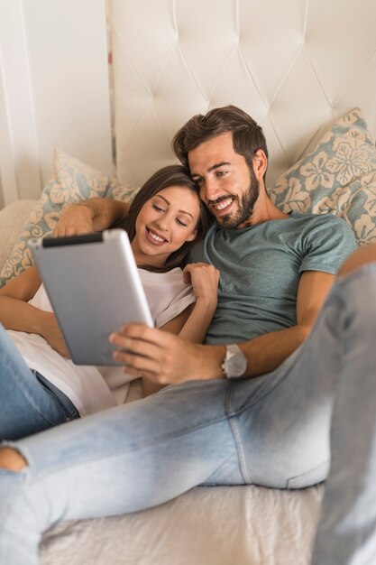 Glückliches Paar, das Tablette auf Bett verwendet