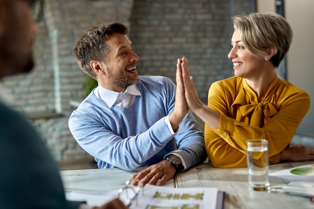 Glückliches Paar feiert und gibt sich Highfive, während es sich bei einem Treffen mit einem Immobilienmakler befindet