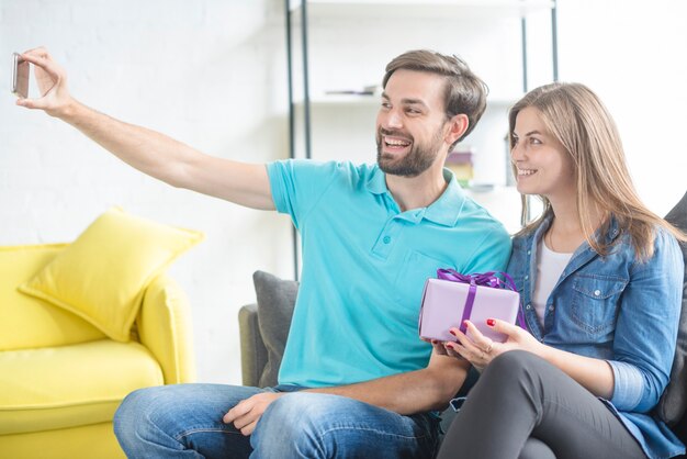 Glückliches Paar mit dem Valentinsgrußgeschenk, das selfie auf Smartphone nimmt