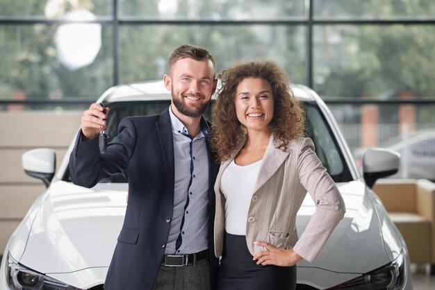 Glückliches Paar posiert mit weißem Neuwagen und Schlüsseln