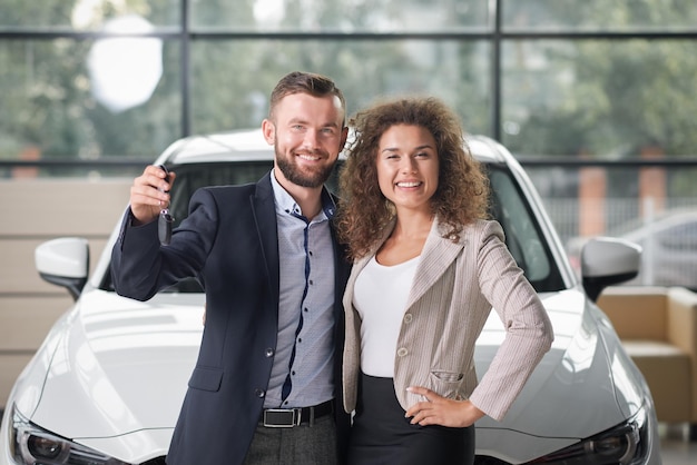 Glückliches Paar posiert mit weißem Neuwagen und Schlüsseln