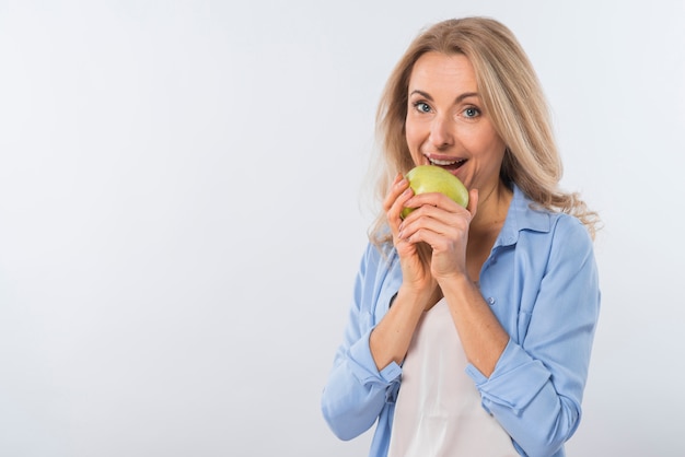 Glückliches Porträt einer lächelnden jungen Frau, die grünen Apfel gegen weißen Hintergrund isst