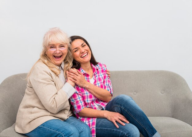 Glückliches Porträt einer Mutter und der Tochter, die auf dem Sofa zusammen lachen sitzen
