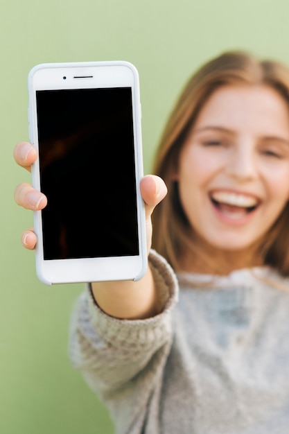 Glückliches Porträt einer schönen jungen Frau, die Smartphone in Richtung zur Kamera hält