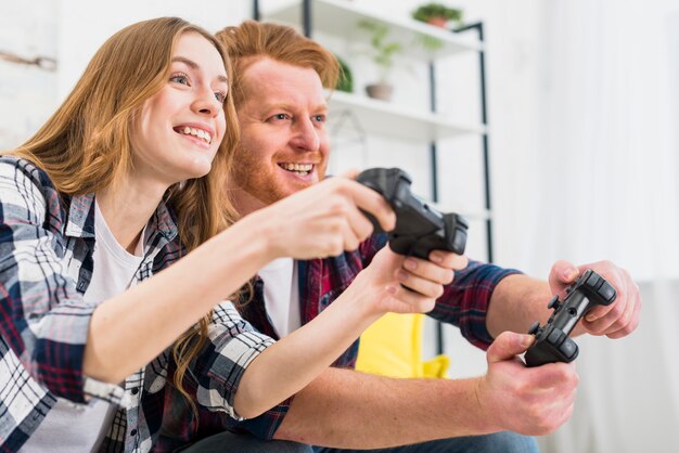 Glückliches Porträt von den jungen Paaren, die Spielkonsole mit Steuerknüppeln spielen