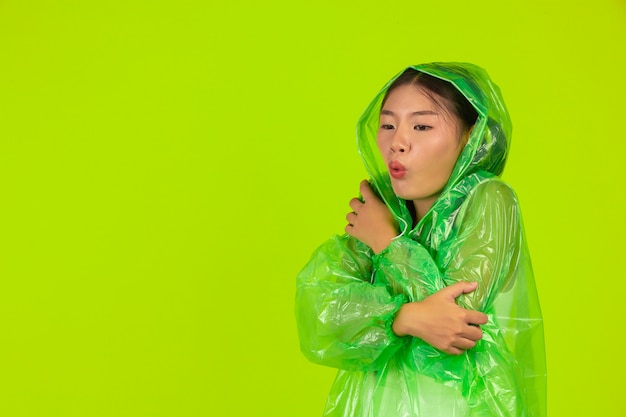 glückliches schönes Mädchen, grüne Kleidung, Regenschirm und Mantel, regnerischer Tag tragend.