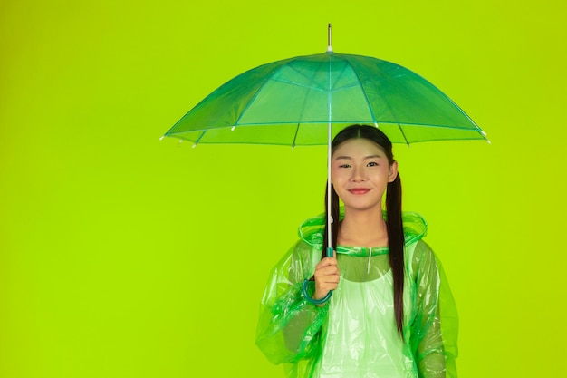 glückliches schönes Mädchen, grüne Kleidung, Regenschirm und Mantel, regnerischer Tag tragend.