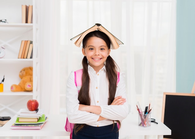 Glückliches Schulmädchen mit Buch auf Kopf