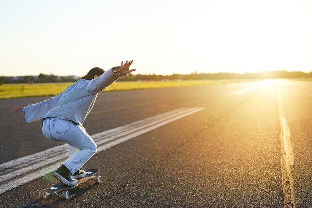 Glückliches skatermädchen, das ihr skateboard fährt und spaß auf einer leeren straße hat, lächelnde frau, die kreuzfahrt genießt