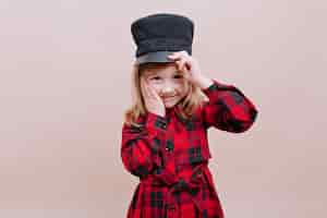 Kostenloses Foto glückliches stilvolles kleines mädchen trägt schwarze mütze und kariertes hemd hält eine mütze und ihre wange mit dem schönen lächeln