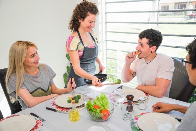 Glückliches Umhüllungslebensmittel der jungen Frau zu ihrem Freund, der auf Tabelle sitzt