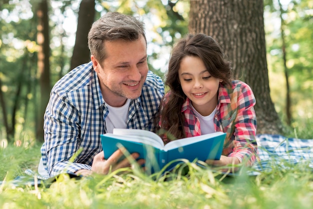 Kostenloses Foto glückliches vater- und tochterlesebuch zusammen am park