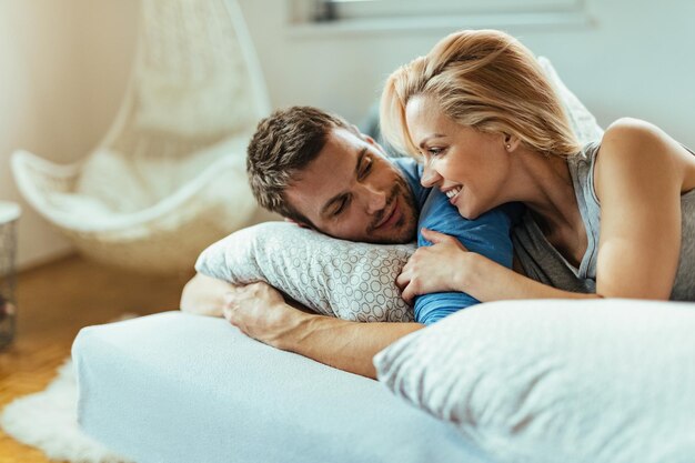 Glückliches verliebtes Paar, das sich morgens beim Entspannen im Schlafzimmer unterhält