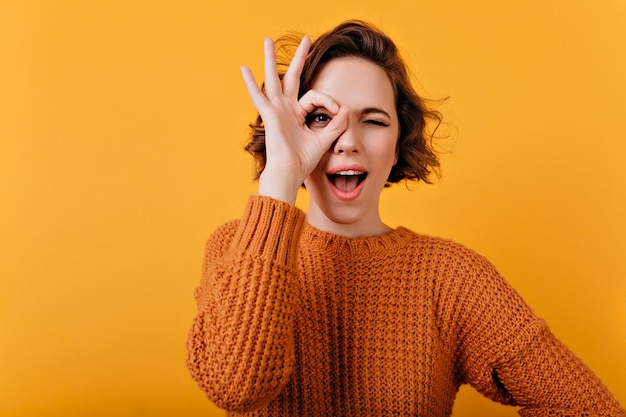 Glückselige junge Frau mit blasser Haut, die lustige Gesichter während des Fotoshootings macht