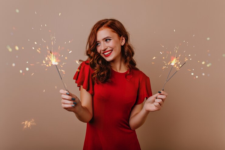Kostenlose Foto glückselige lockige frau mit wunderkerzen, die weihnachtszeit genießen. innenfoto des lachenden hübschen mädchens mit bengalischen lichtern.