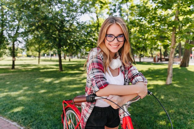 Glückselige süße Dame mit dem Fahrrad, das mit Lächeln schaut. Außenaufnahme des herrlichen weißen Mädchens, das Wochenende im Frühling genießt.