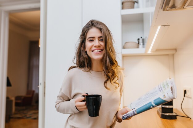 Glückseliges Mädchen, das Glück ausdrückt und Kaffee in ihrer gemütlichen Küche trinkt