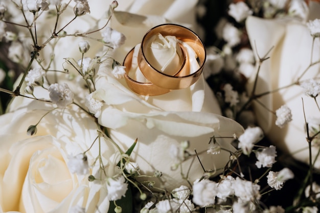 Goldene Eheringe auf der weißen Rose vom Hochzeitsblumenstrauß