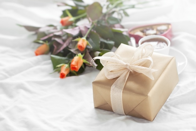 Goldene Geschenk-Paket mit einem Strauß Blumen und Pralinen