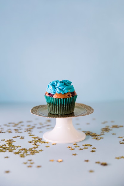 Kostenloses Foto goldene sterne verbreiteten über dem frischen geschmackvollen geburtstagkleinen kuchen auf cakestand auf blauem hintergrund