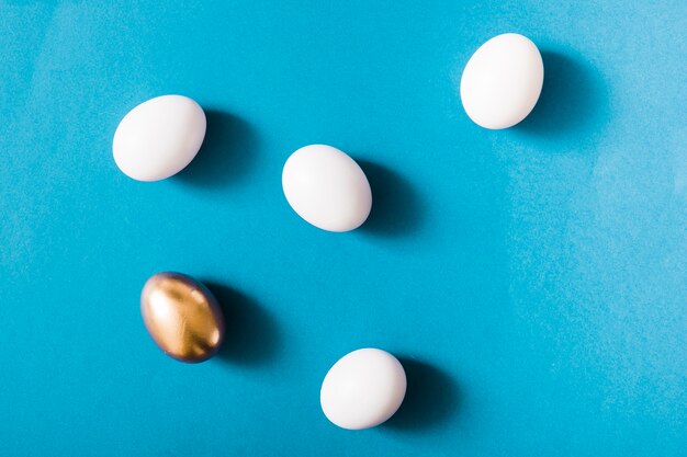 Goldenes Ei und weiße Eier auf blauem Hintergrund