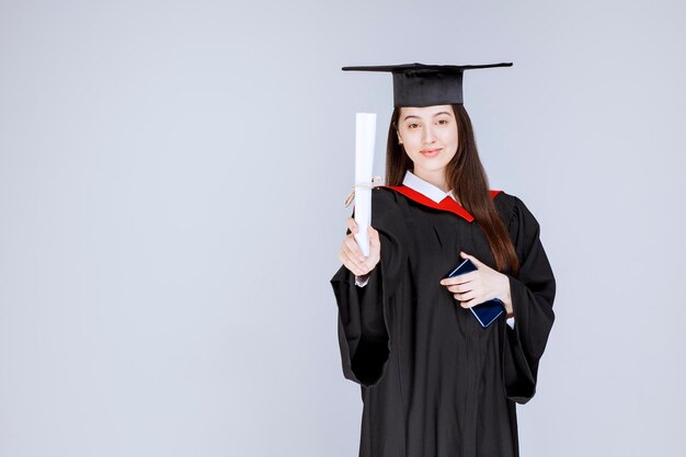 Graduate Student im Kleid Handy in der Hand mit Diplom. Foto in hoher Qualität
