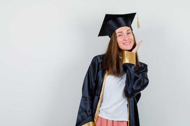 Graduierte Frau, die mit Hand nahe Gesicht in Freizeitkleidung, Uniform und zart aussehend aufwirft. Vorderansicht.