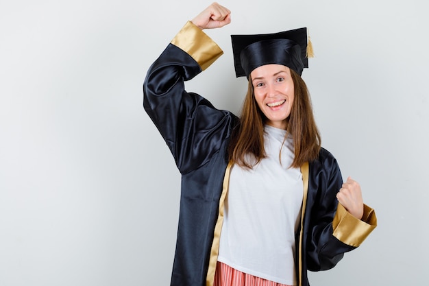 Graduierte Frau, die Siegergeste in Freizeitkleidung, Uniform zeigt und glückselig aussieht, Vorderansicht.