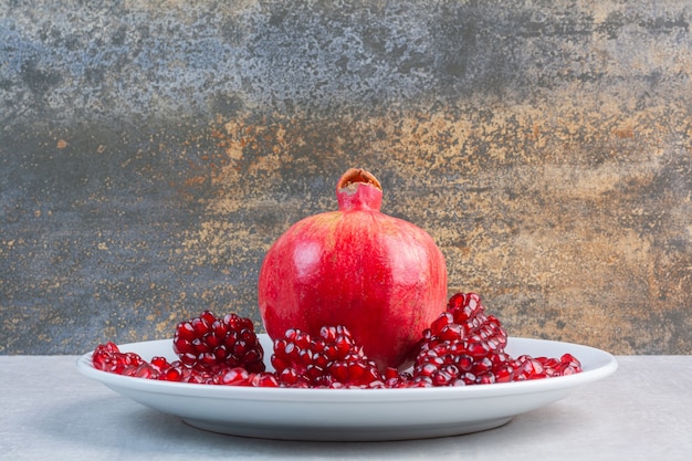 Granatapfel und Arillen auf einem Teller, auf dem gemischten Tisch.