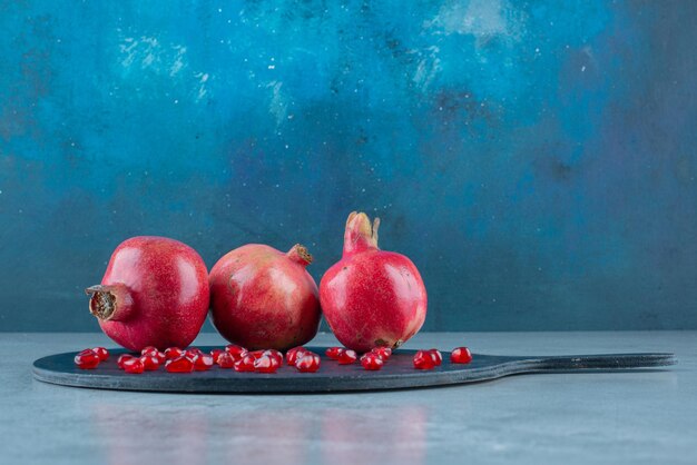 Granatapfel und rote Samen auf einer schwarzen Servierplatte.