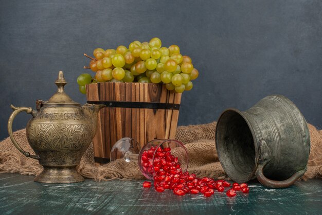 Granatapfelkerne und Eimer Trauben auf Marmortisch mit Vase und Teekanne.