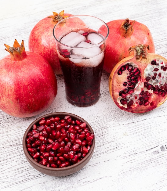 Granatapfelsaft mit eiswürfeln und granatapfel auf weißem holztisch