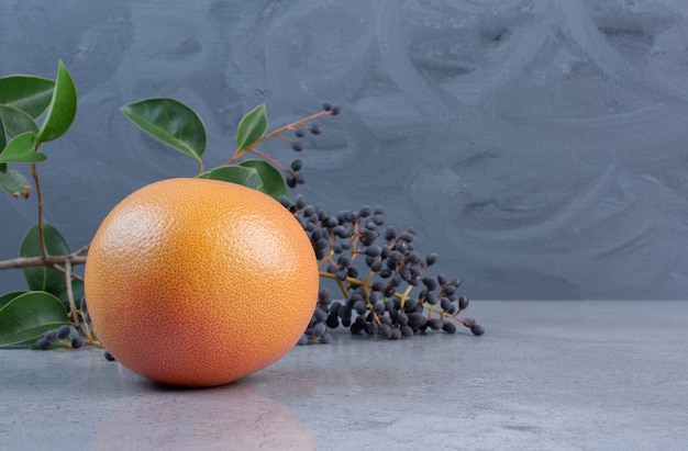 Grapefruit neben dekorativem Zweig mit Beeren und Blättern auf Marmorhintergrund.