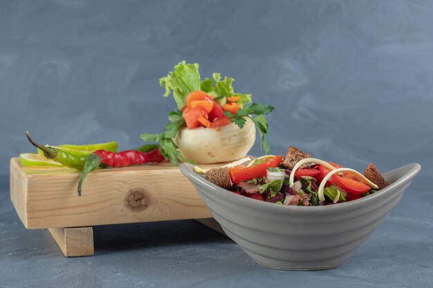 Graue Salatschüssel neben einem Bündel Gemüse auf einem Holzbrett auf Marmortisch.