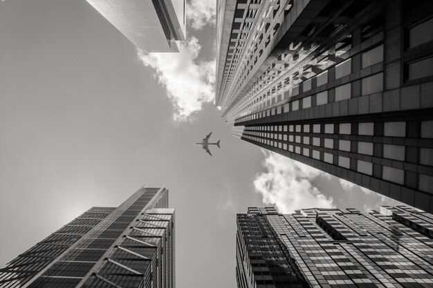 Graustufenaufnahme des niedrigen Winkels eines Flugzeugs, das über Hochhäusern fliegt