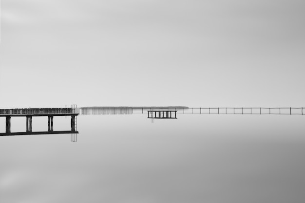 Graustufenaufnahme eines hölzernen Piers nahe dem Meer unter dem schönen bewölkten Himmel