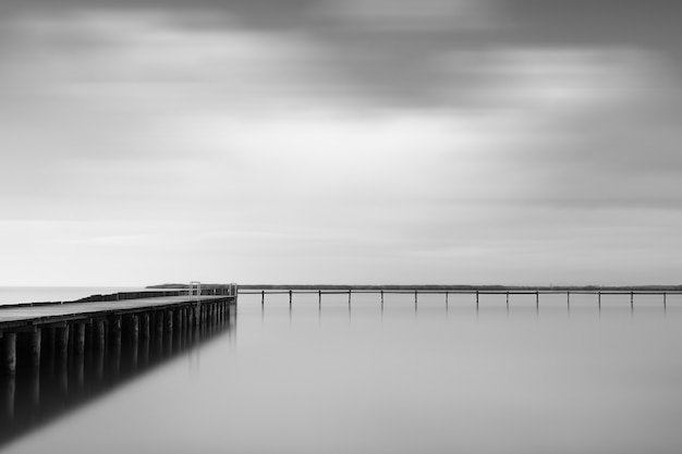 Kostenloses Foto graustufenaufnahme eines hölzernen piers nahe dem meer unter dem schönen bewölkten himmel