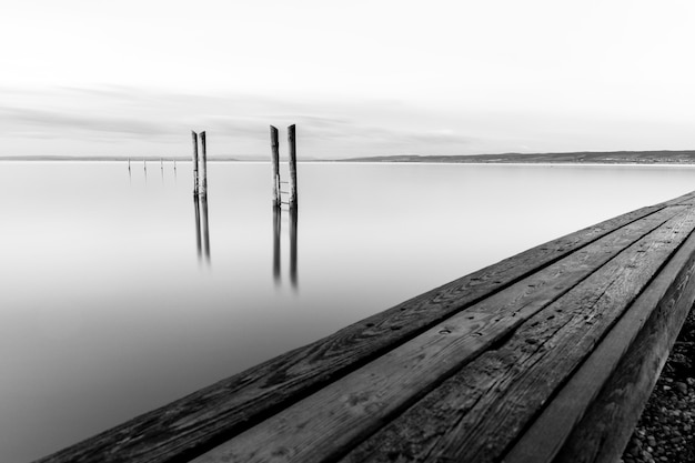 Graustufenaufnahme eines hölzernen Piers nahe dem Meer unter dem schönen bewölkten Himmel